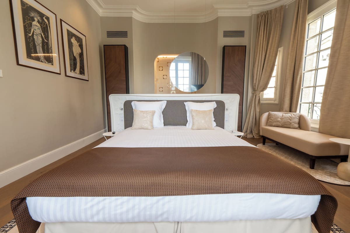A spacious bedroom with a large bed, a sofa, and a mirror.