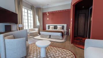 A modern hotel room with a large bed, two armchairs, a round coffee table, and a television.