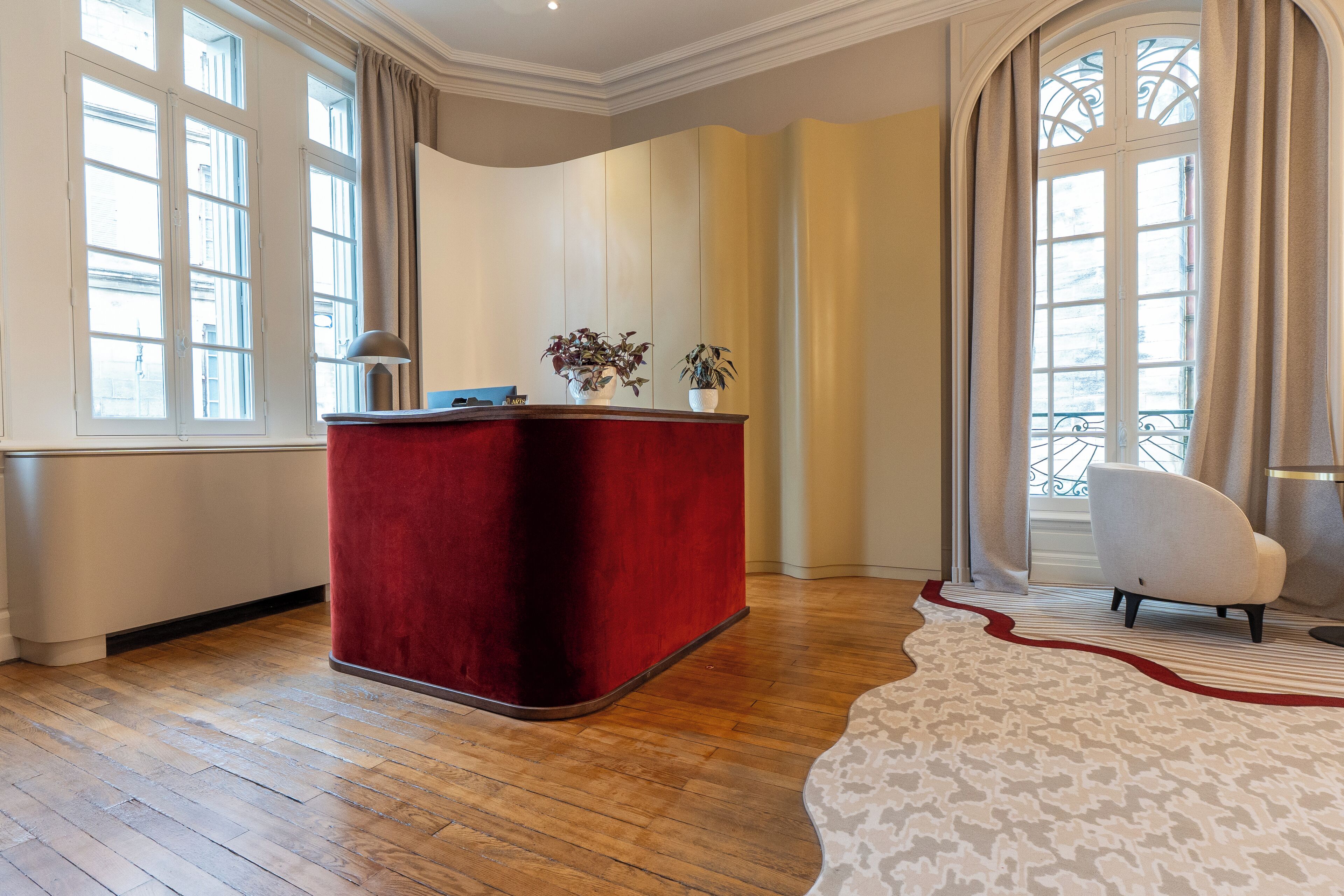 A room with a red velvet reception desk, a white armchair, and a patterned rug.