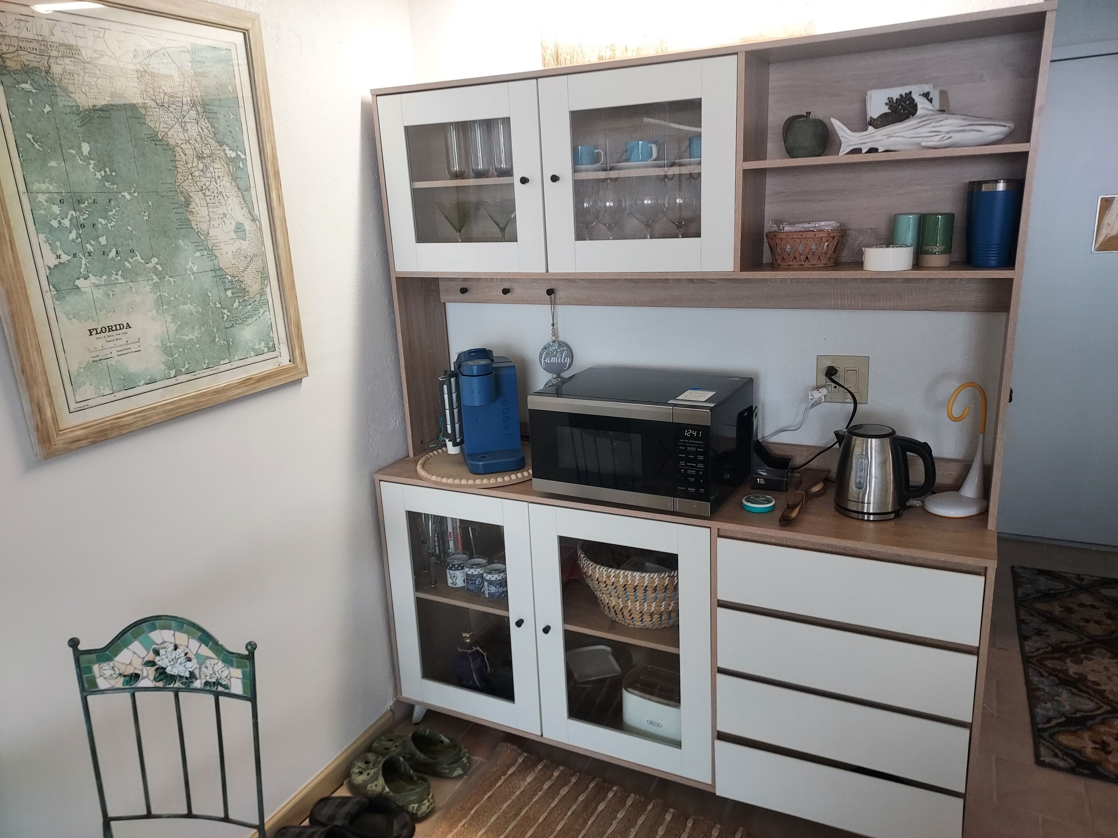 Una cocina con un mapa, armarios, un microondas y un hervidor.