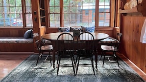 A wooden dining area with a round table and chairs, large windows with a view of the outside, and a hanging light fixture. - Two charming cottages, a quiet ocean cove, a serene forest with private trails (Phippsburg)