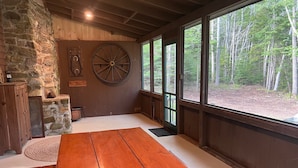 A rustic interior with a stone wall, wooden beams, a large wooden table, and a view of a forest through large windows. - Two charming cottages, a quiet ocean cove, a serene forest with private trails (Phippsburg)