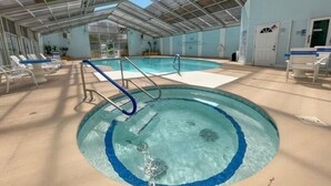 Una piscina con tetto in vetro, circondata da poltrone relax e un ingresso.