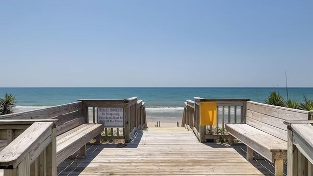Una passerella in legno che conduce a una spiaggia, con un cartello che indica proprietà privata e divieto di accesso.