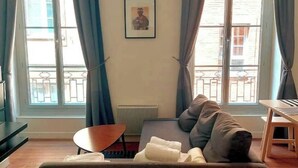 Un salón con sofá, una mesita y una ventana con cortinas.