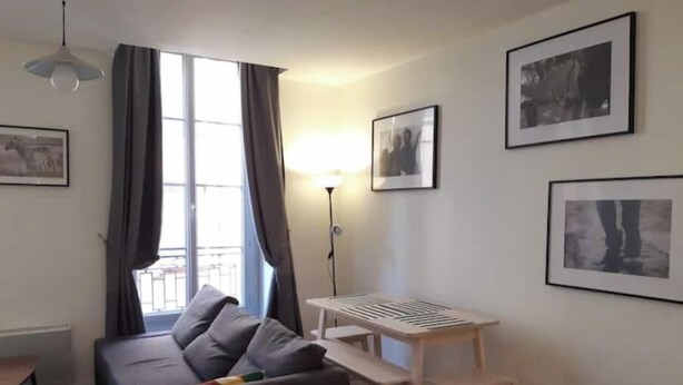 Una sala de estar moderna con un sofá, una mesa de madera y una lámpara de pie. Hay cuadros enmarcados en las paredes.