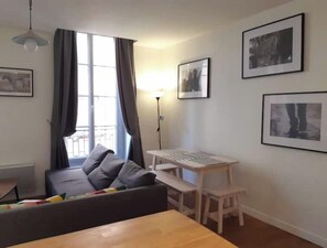 A modern living room with a sofa, a wooden table, and a standing lamp. There are framed pictures on the walls.