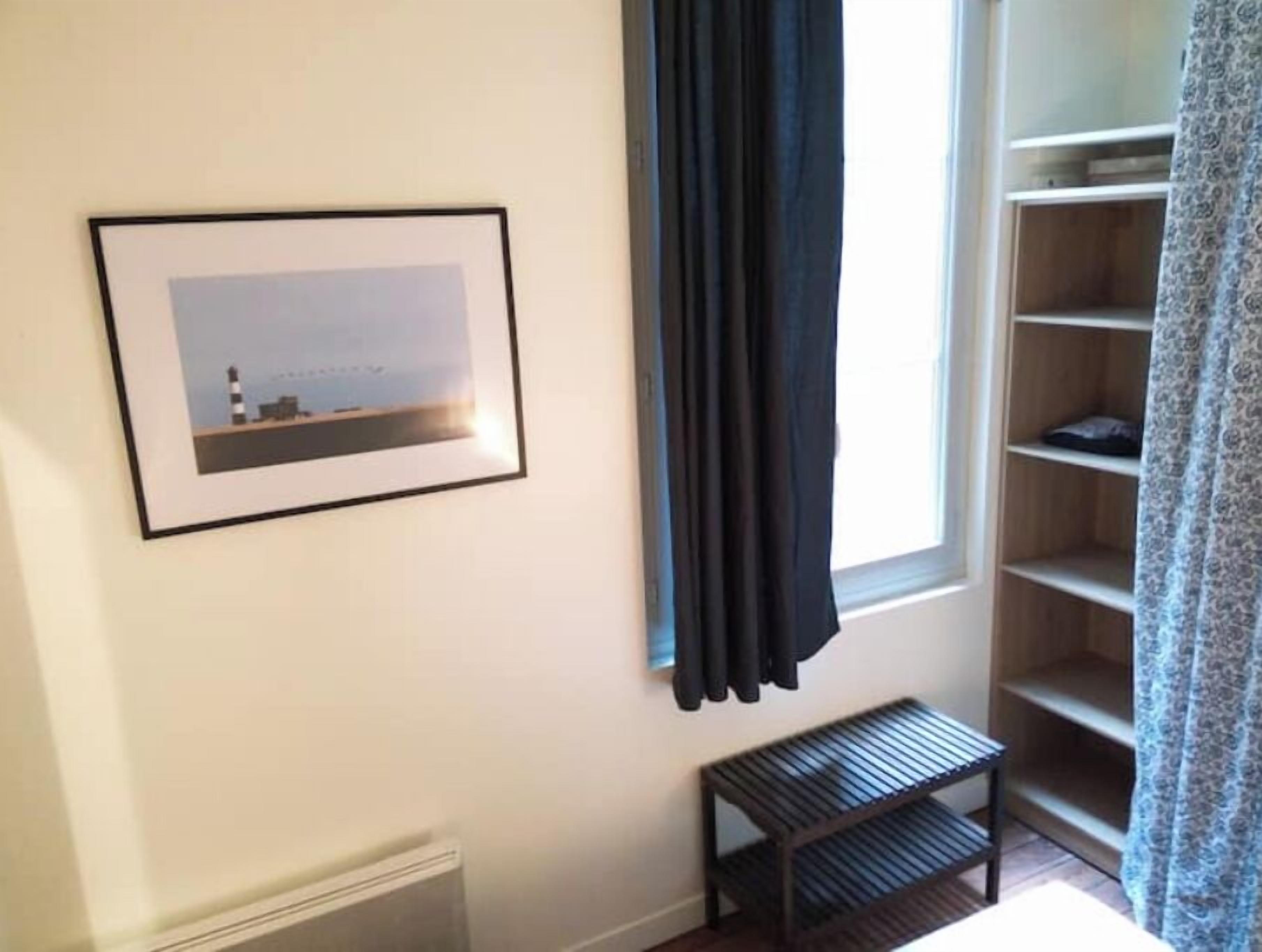 Ein Zimmer mit einem gerahmten Bild eines Leuchtturms, einem dunklen Vorhang, einer Holzbank und einer eingebauten Regaleinheit.