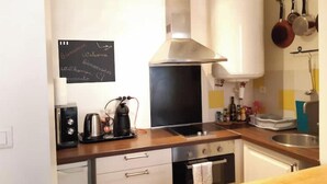 Una cocina moderna con estufa, horno y cafetera. Hay una pizarra con escritura en la pared y un calentador de agua sobre la estufa.