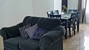 Ein modernes Wohnzimmer mit einem dunkelgrauen Sofa, einem Esstisch mit Stühlen, einer Treppe und einer Wanduhr.