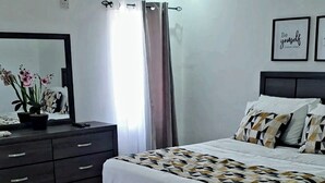Ein Schlafzimmer mit einem Bett, einem Schminktisch, einem Spiegel und einer Wand mit zwei gerahmten Motivationssprüchen.