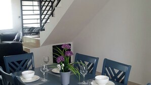 Ein Essbereich mit Tisch für vier Personen, umgeben von blauen Stühlen, einer Treppe und Blick auf ein Wohnzimmer.