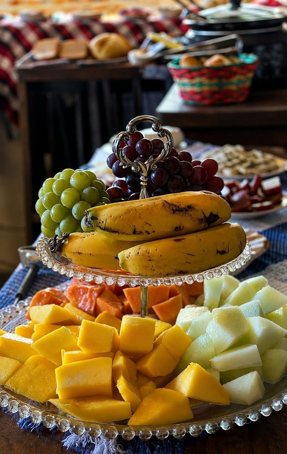 Ett fat med olika frukter, bland annat bananer, vindruvor, mango och melon, som står på ett genomskinligt underlägg.