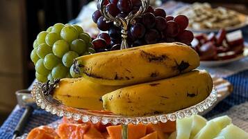 Ett fat med olika frukter, bland annat bananer, vindruvor, mango och melon, som står på ett genomskinligt underlägg.
