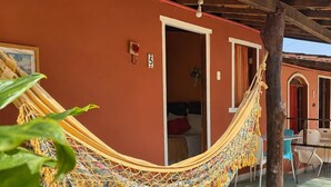 A hammock tied between two wooden beams, a door leading to a room, and a small table with chairs outside a building with a tiled roof. - Pousada Princesa da Serra (Santana do Riacho)