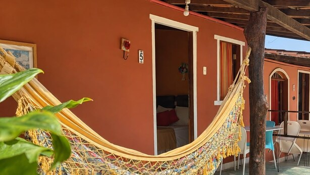 A hammock tied between two wooden beams, a door leading to a room, and a small table with chairs outside a building with a tiled roof. - Pousada Princesa da Serra (Santana do Riacho)