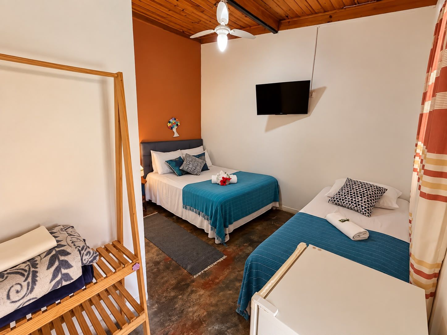 A bedroom with two beds, a TV mounted on the wall, and a wooden ceiling.