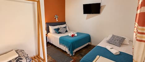 A bedroom with two beds, a TV mounted on the wall, and a wooden ceiling.