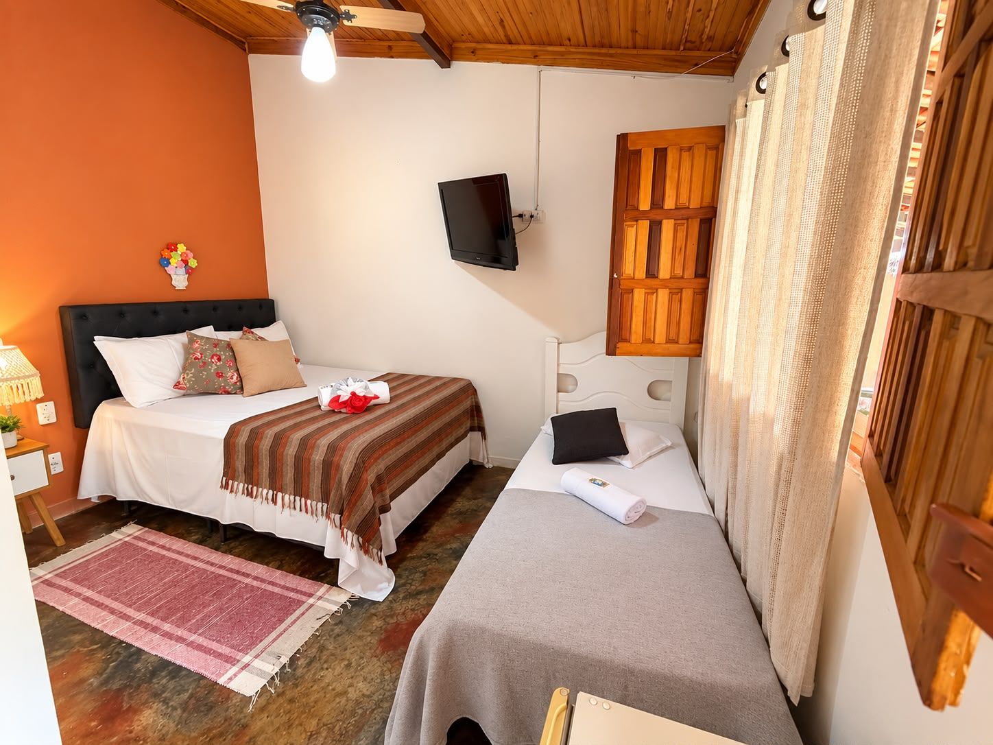 Een hotelkamer met twee bedden, een televisie, een houten plafond en een raam met gordijnen.