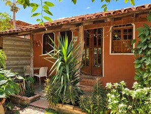 A house with a tiled roof, a wooden door, and a small patio area with chairs and plants. - Pousada Princesa da Serra (Santana do Riacho)