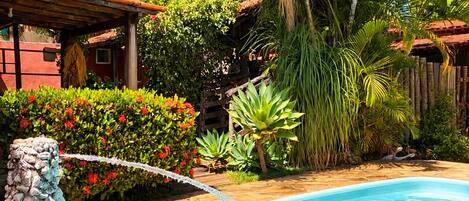 Une piscine bordée d’un mur en pierre, entourée de plantes tropicales et agrémentée d’une pergola en bois.