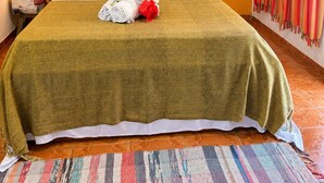 A hotel room with a wooden headboard, a bed with white and red pillows, a green blanket, and a colorful woven rug. - Pousada Princesa da Serra (Santana do Riacho)