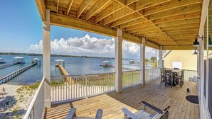A wooden deck with a view of the water, a covered seating area, and a building in the background. - Lux 6BR, Lagoon Front, Private Heated Pool, Gulf Views, Boat Dock, Walk To Beach (Gulf Shores)