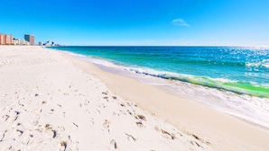 A beach with footprints leading to the water, a clear sky, and buildings in the background. - Lux 6BR, Lagoon Front, Private Heated Pool, Gulf Views, Boat Dock, Walk To Beach (Gulf Shores)
