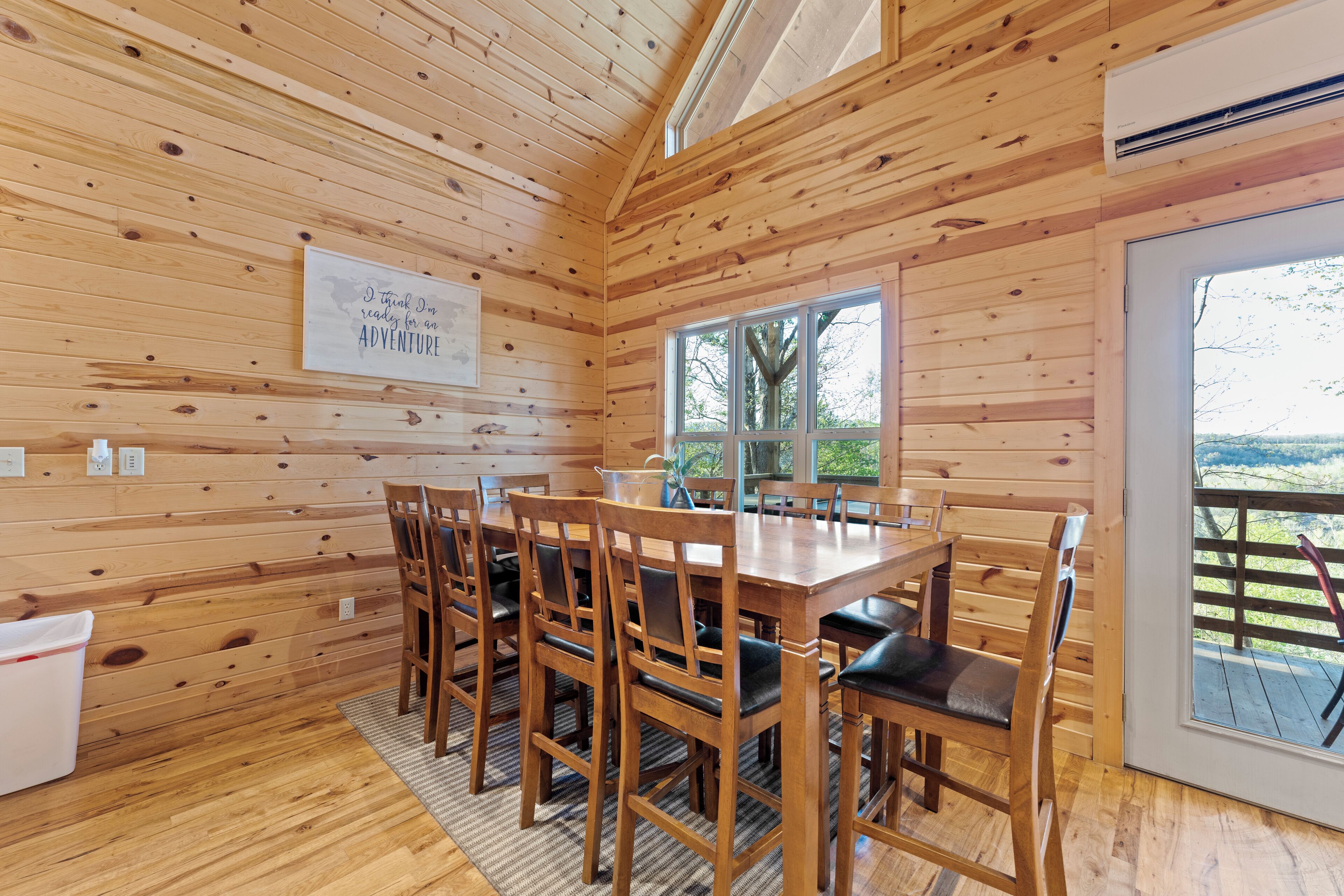 Una cabaña de madera con comedor que presenta una mesa grande y sillas, una ventana con vistas al exterior y un cartel en la pared.