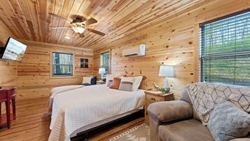 A wooden cabin bedroom with a bed, a sofa, a TV, and a ceiling fan.