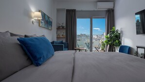 A modern hotel room with a large bed, a sofa, a small table, and a balcony with a view of the city.