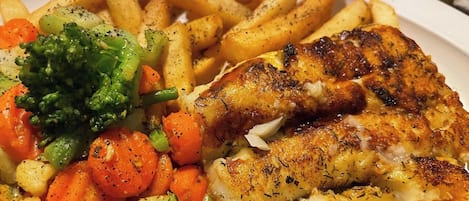 Un plato con pescado a la plancha, papas fritas y verduras mixtas.