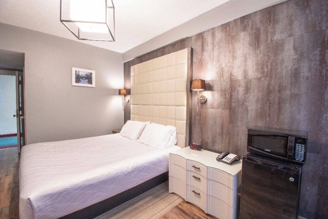 A bedroom with a bed, bedside table, lamp, and a microwave.