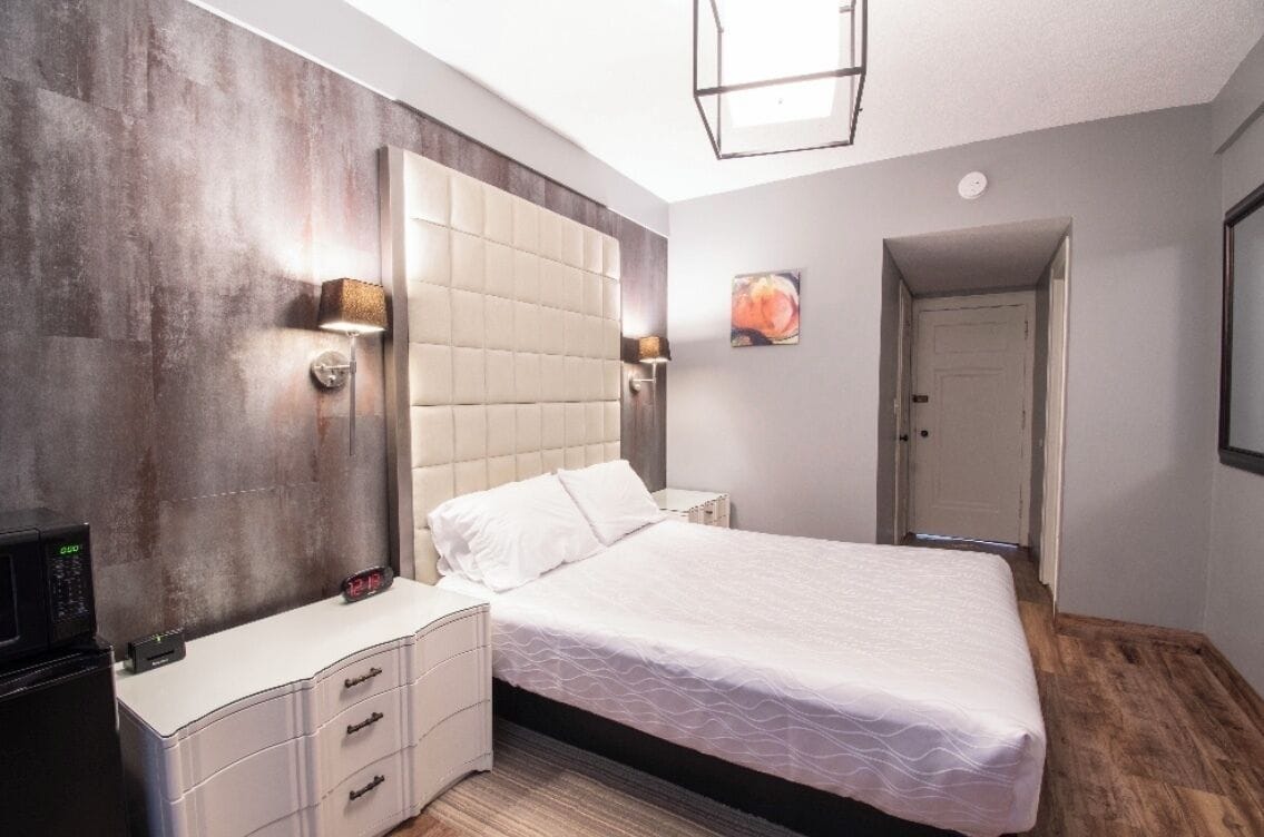 A modern bedroom with a large bed, bedside lamps, a nightstand, and a built-in TV.