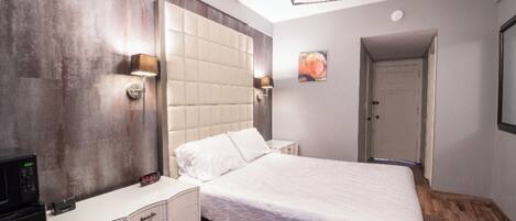 A modern bedroom with a large bed, bedside lamps, a nightstand, and a built-in TV.