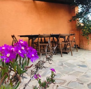 En terrasse med et bord og stole, en stengulv og en væg med slyngplanter.