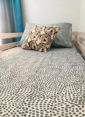 En seng med et mønstret sengetæppe og to puder, hvoraf den ene har et swirlsdesign og den anden et leopardmønster.