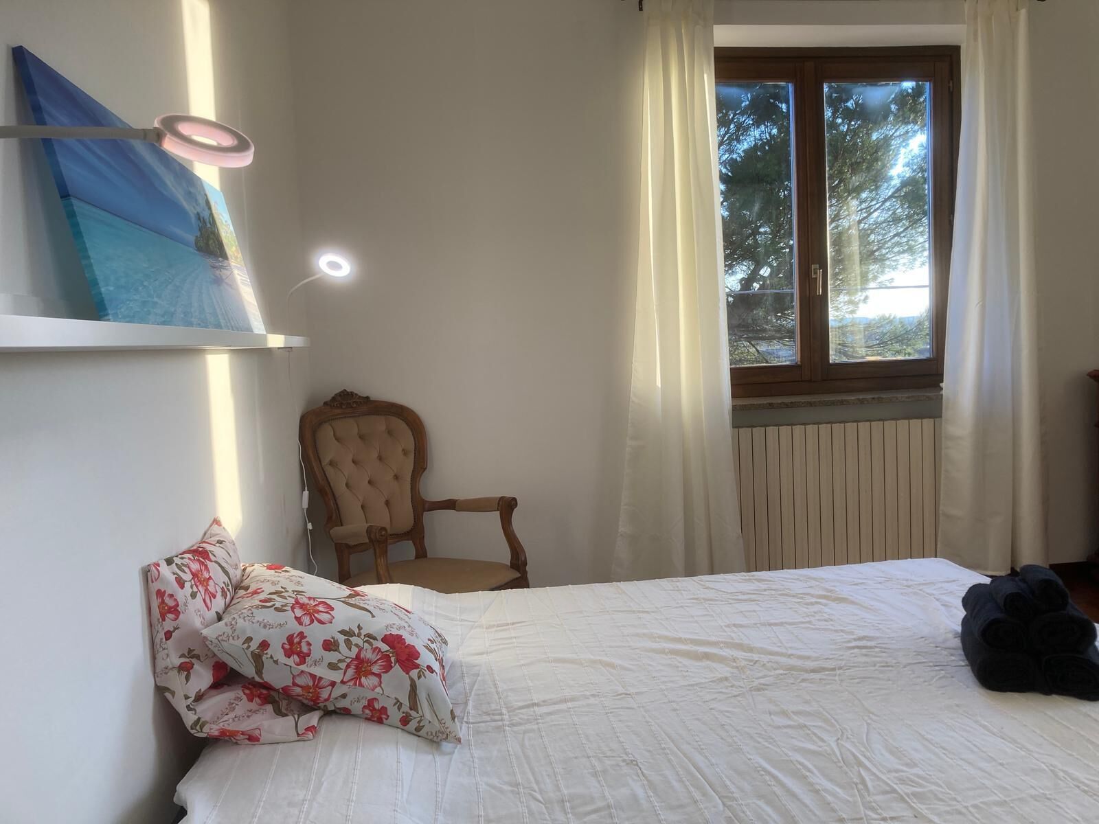 A bedroom with a bed, a chair, a window with curtains, and a painting on the wall.