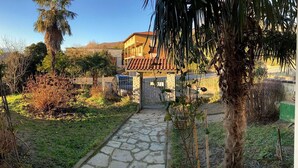 Una casa con un sendero de piedra que conduce a una entrada con reja, rodeada de abundante vegetación y un cielo despejado.