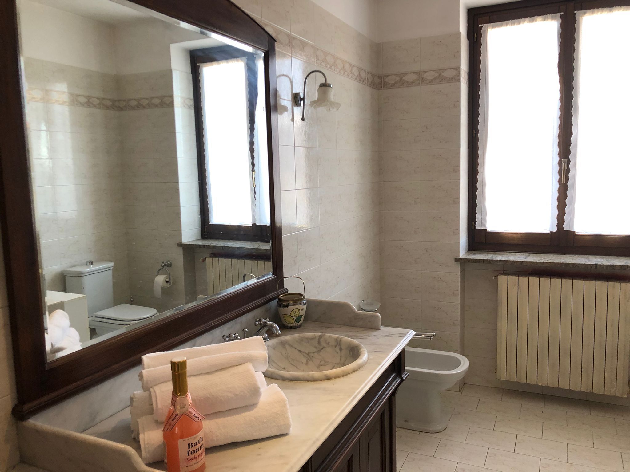 Un baño con lavamanos de mármol, un espejo grande, un inodoro y un bidé.