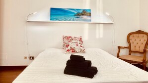 Una cama bien hecha con una toalla doblada, una almohada floral y un cuadro de una playa en la pared de arriba.