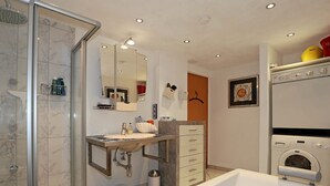Un baño moderno con cabina de ducha, lavamanos con espejo, inodoro y lavadora integrada.