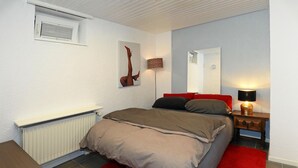 Un dormitorio con una cama, una mesita de noche, una lámpara, un radiador, una ventana y un espejo montado en la pared.