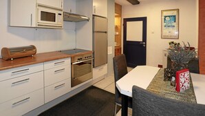 Cocina compacta equipada con microondas, horno y refrigerador. Hay una mesa de comedor con sillas y un florero decorativo.