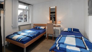 Una habitación de hotel con dos camas, un escritorio, una silla, un espejo y una ventana con persianas.