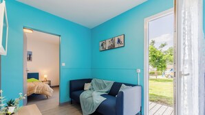 A room with a teal wall, a dark blue sofa, a wooden table with a vase, and a view of a playground through a glass door.