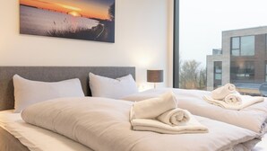 Een hotelkamer met twee bedden, een groot raam en een schilderij van een zonsondergang aan de muur.