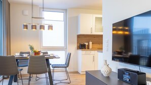 Een moderne keuken met witte kasten, een houten aanrecht en een ingebouwde oven. Er is een eethoek met een tafel en stoelen, en een grote flatscreen televisie aan de muur bevestigd.