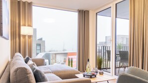 Een moderne woonkamer met een bank, fauteuils, een salontafel en uitzicht op de stad door grote ramen.