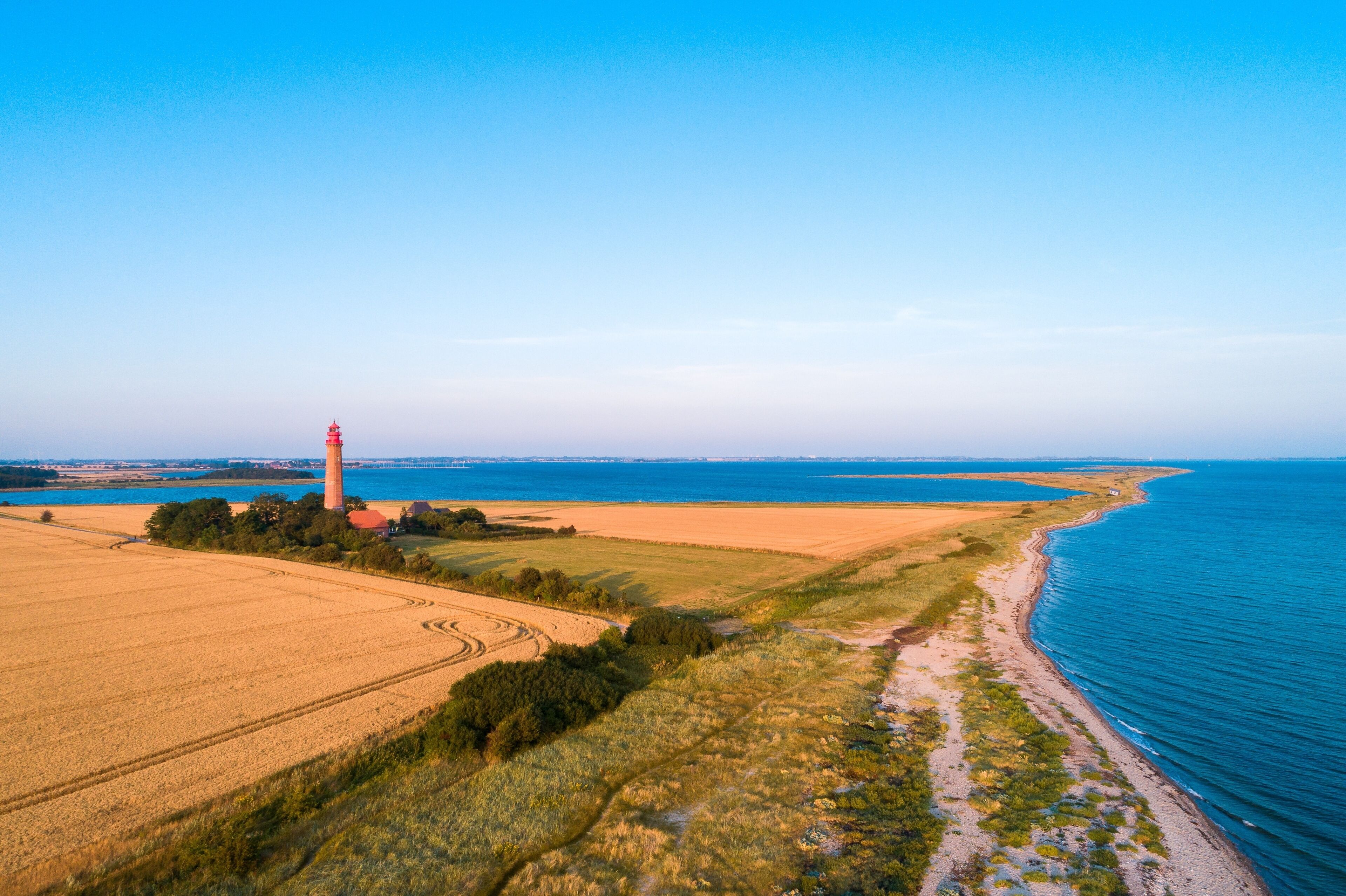Un paysage côtier avec un phare, des champs et une plage.
